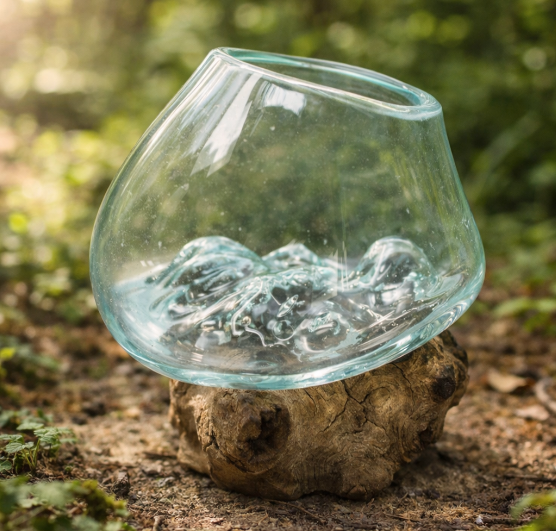 Glazen terrarium gebeeldhouwd interieur, geplaatst op een verweerde houten sokkel buiten te midden van groen.