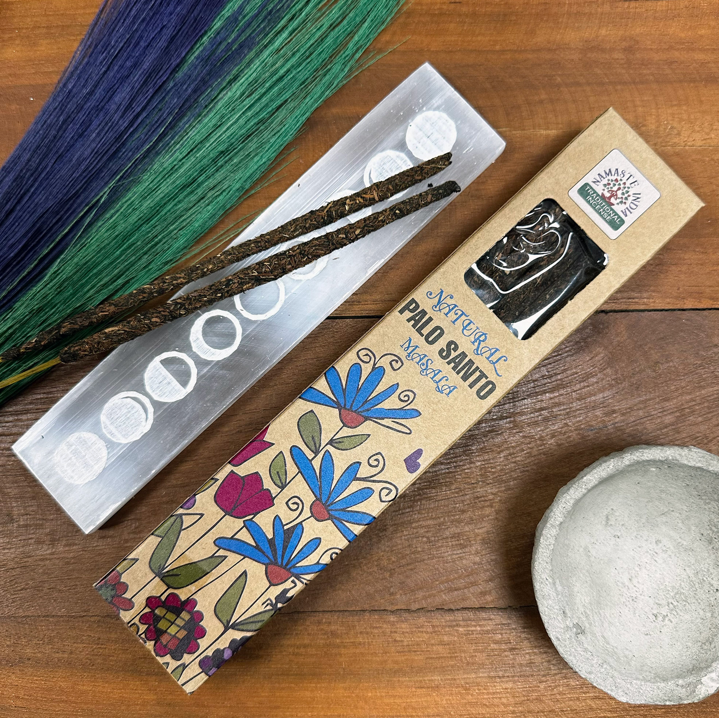 Palo Santo wierook met een seleniet houder en decoratieve botanische elementen, op een houten ondergrond.