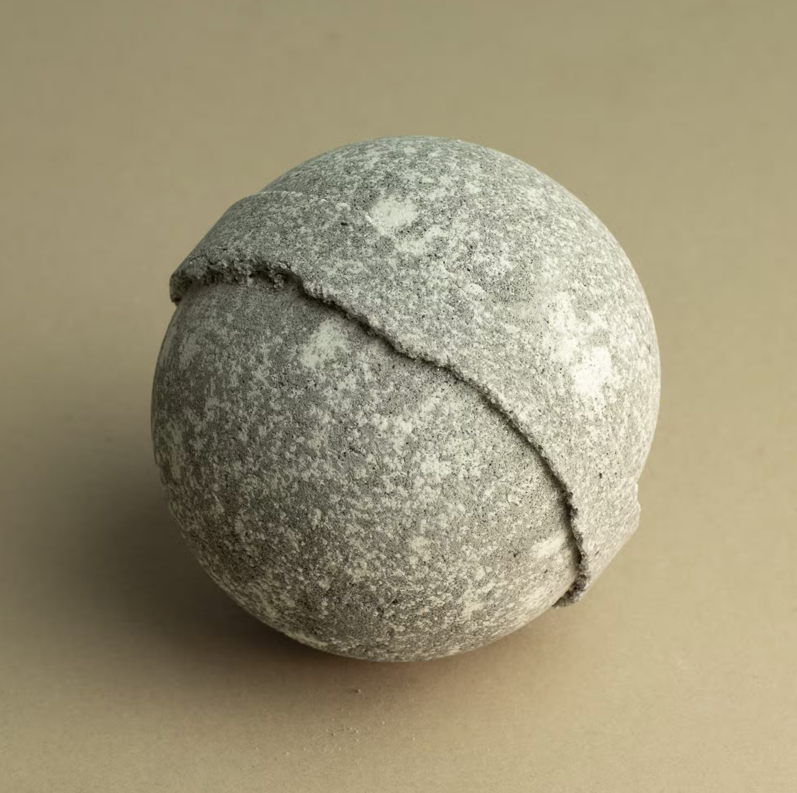 Grijze bol van structuursteen met een donkere gebogen naad op een beige achtergrond