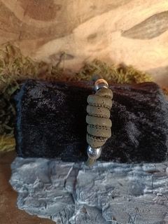 Een opgerold, lichtbruin kleiobject met metalen uiteinden, geplaatst tegen een achtergrond van rotsen en mos.