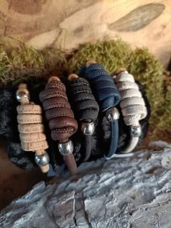Een groene en zilveren armband rust op een donkere rots met mos op de achtergrond.
