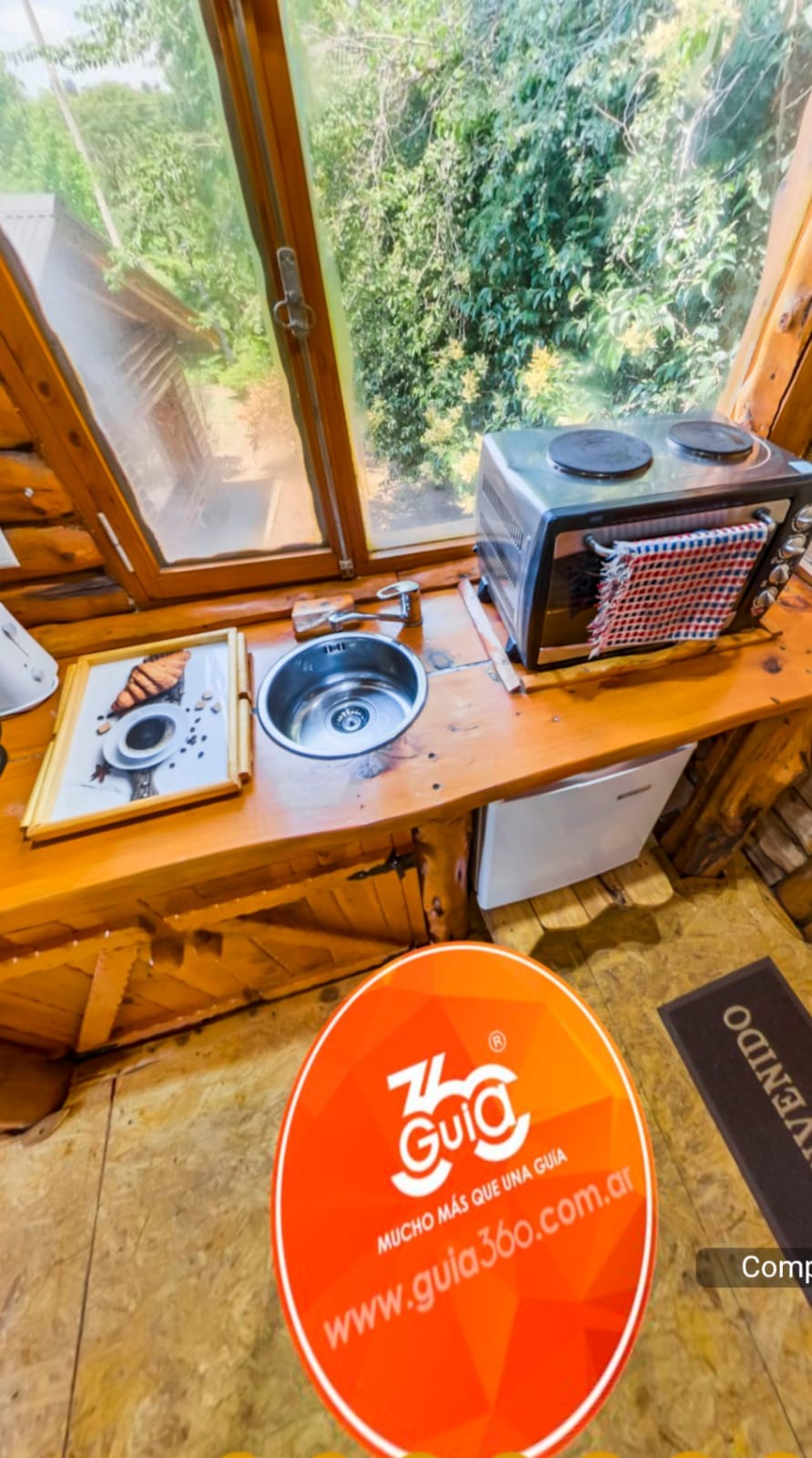 Encimera de madera junto a la ventana con una estufa portátil, fregadero y letrero naranja de “The Giga” en el suelo.