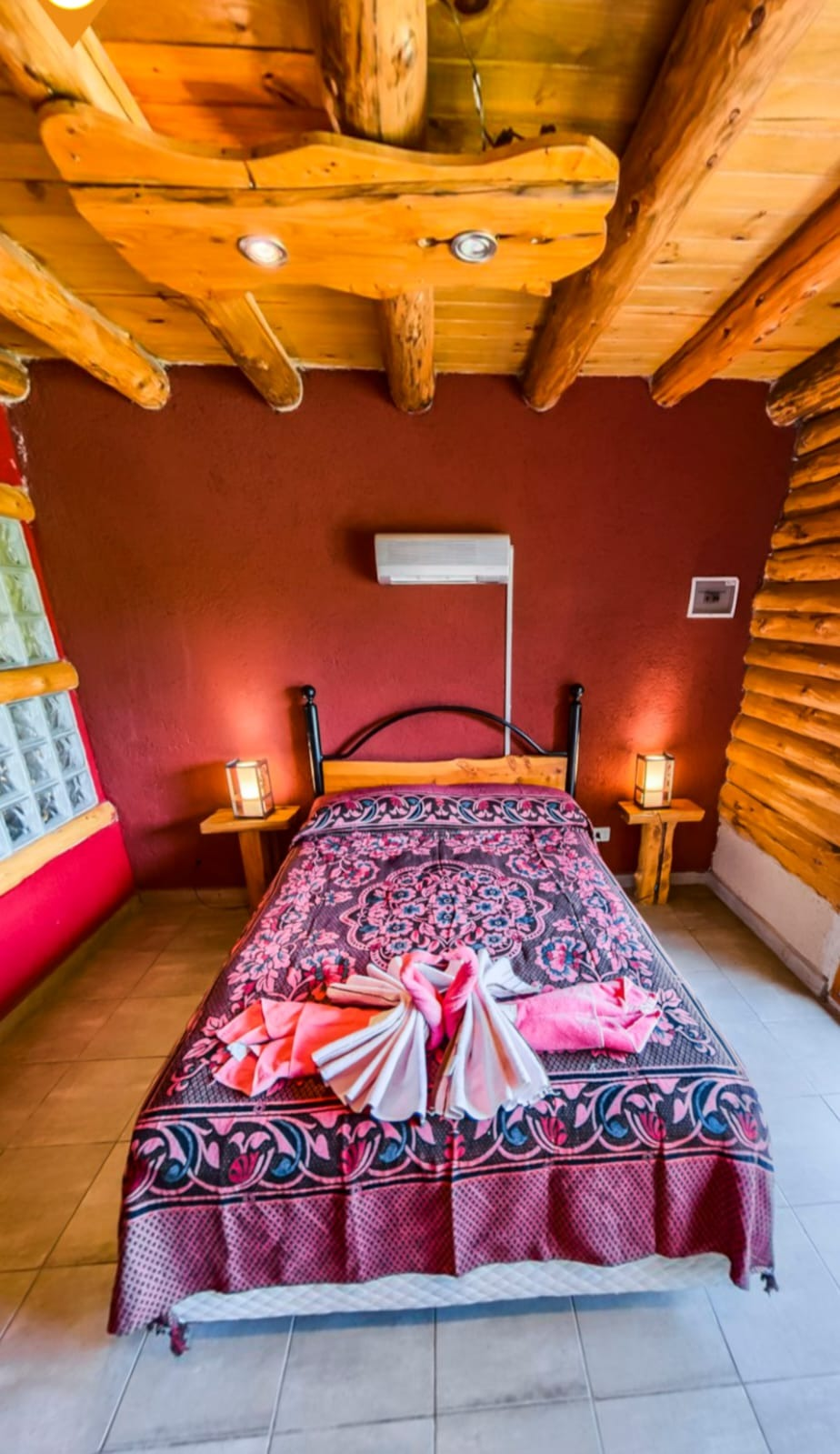 Acogedora habitación rústica con cama doble, paredes rojas, techo de madera y lámparas de noche.