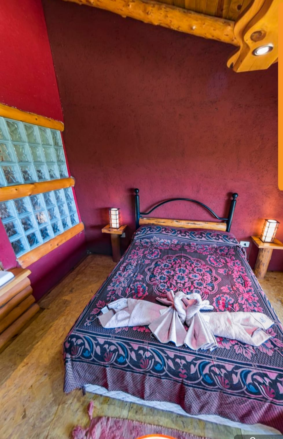 Acogedora habitación con cama doble, colcha estampada y cálidas paredes rojas bajo un techo rústico.
