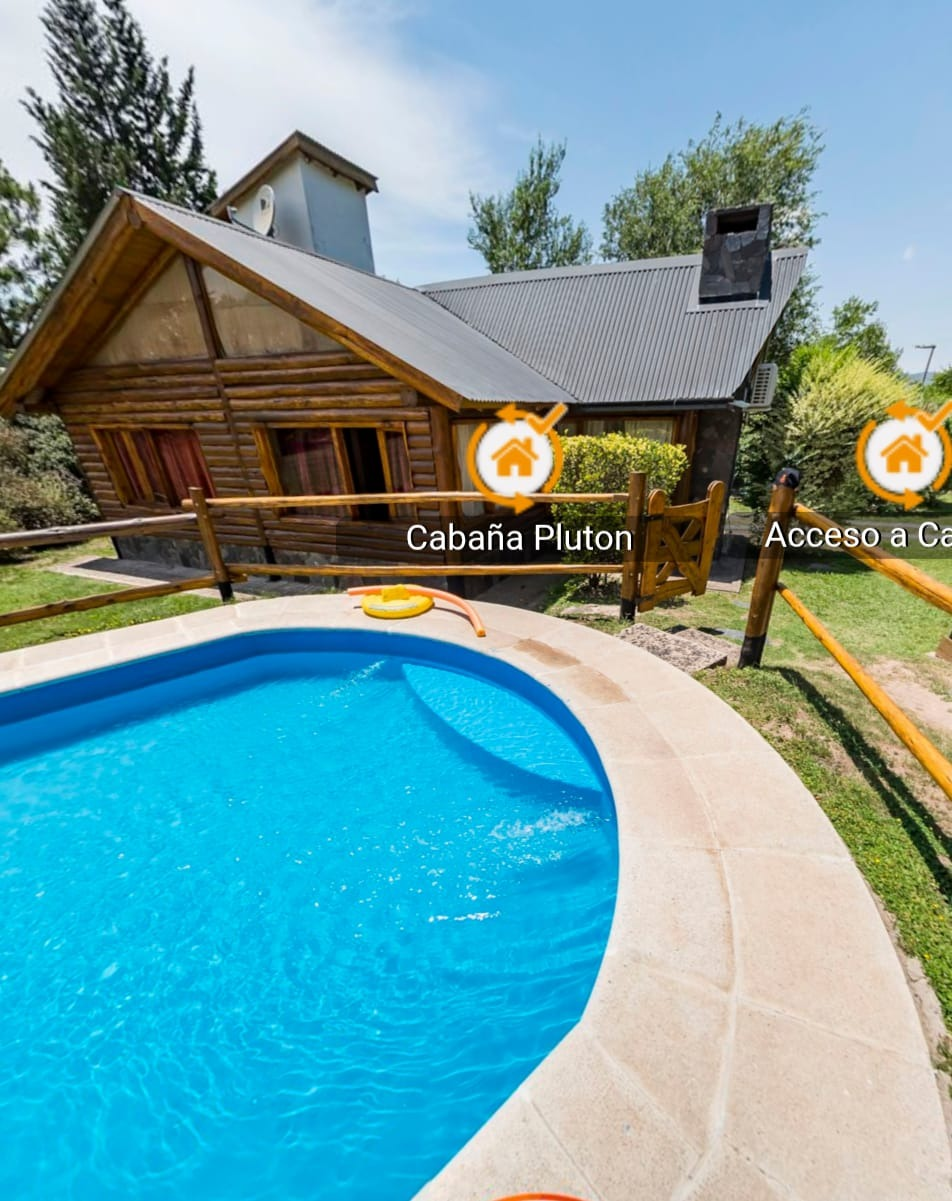 Cabaña de madera junto a una piscina azul con una terraza curva y árboles al fondo.