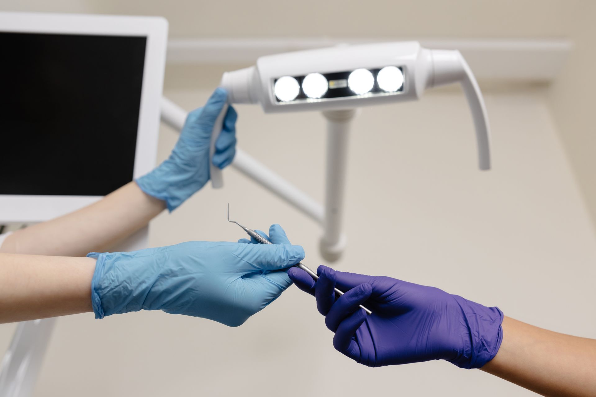 Gloved hands passing a dental tool under an exam light in a clinic