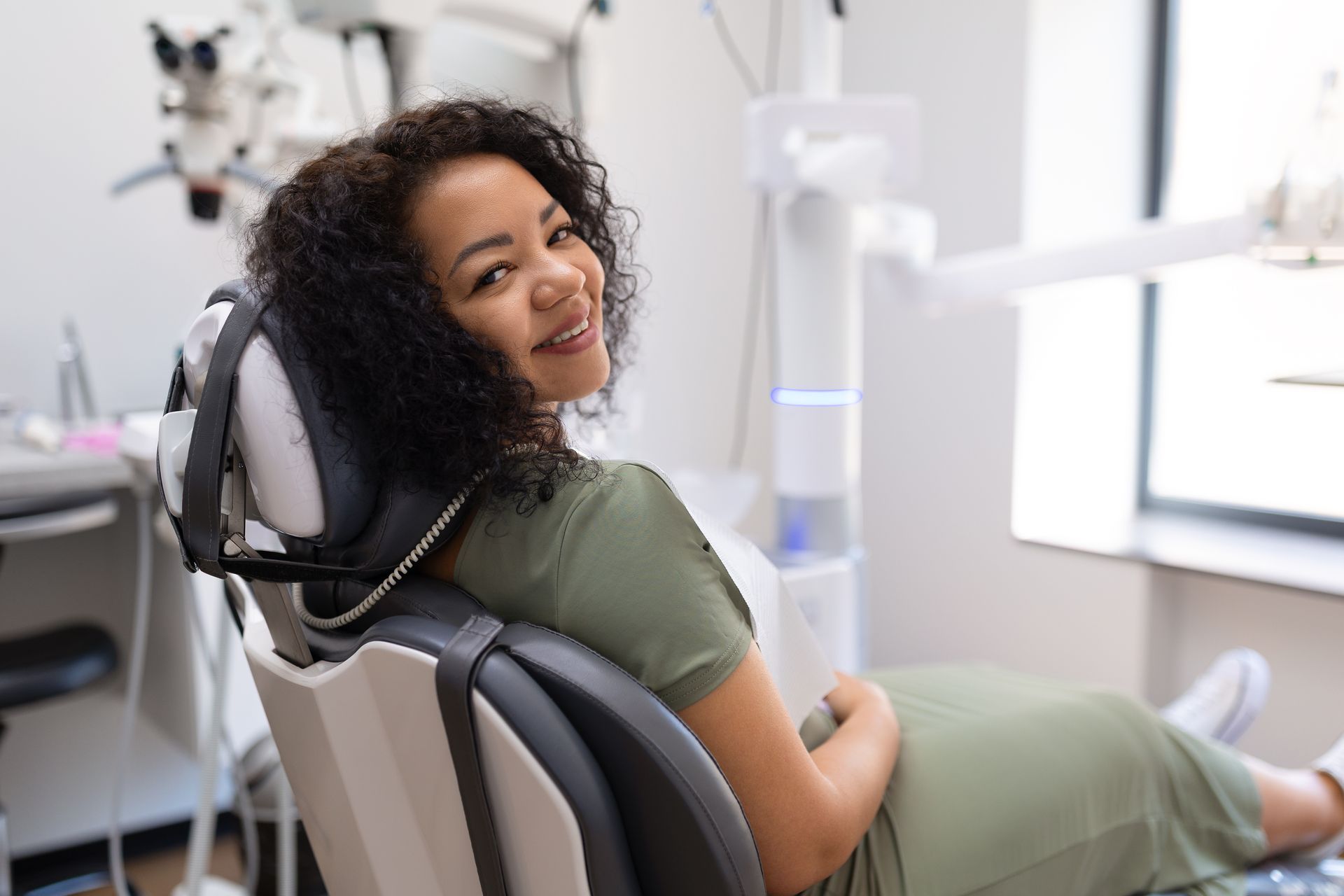 Person reclining in a dental chair, smiling during a dental exam in a bright clinic.