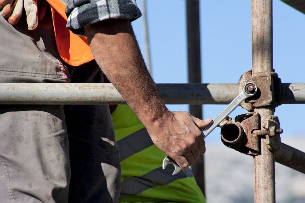 A Man Is Working On A Scaffolding With A Wrench — Fahlstrom Scaffolding Cairns Pty Ltd in Cairn, QLD