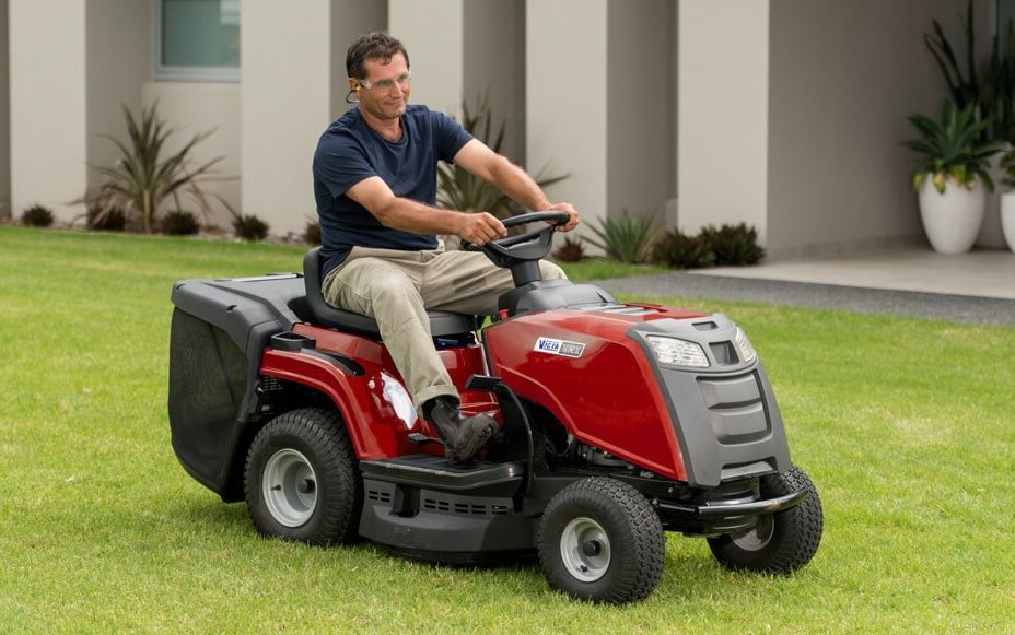 A Man is Riding a Red Lawn Mower on a Lush Green Lawn — Stockers & Partridge In Maitland, NSW