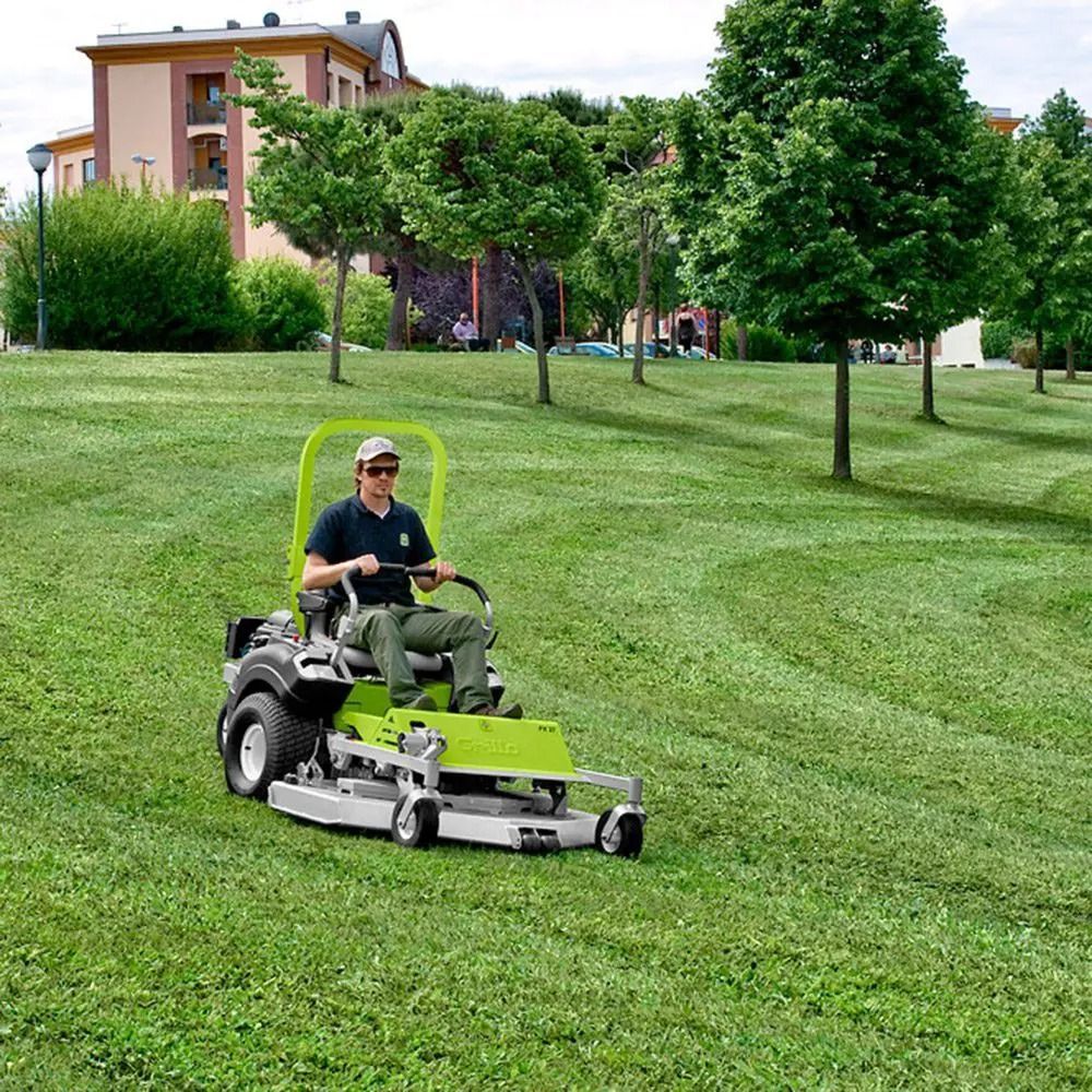 Person mowing a green lawn with a riding mower in a park-like yard near houses and trees — Stockers & Partridge In Raymond Terrace, NSW