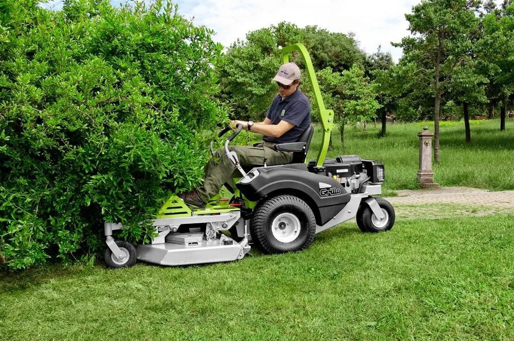 Person operating a riding mower trimming a hedge in a green lawn — Stockers & Partridge In Raymond Terrace, NSW