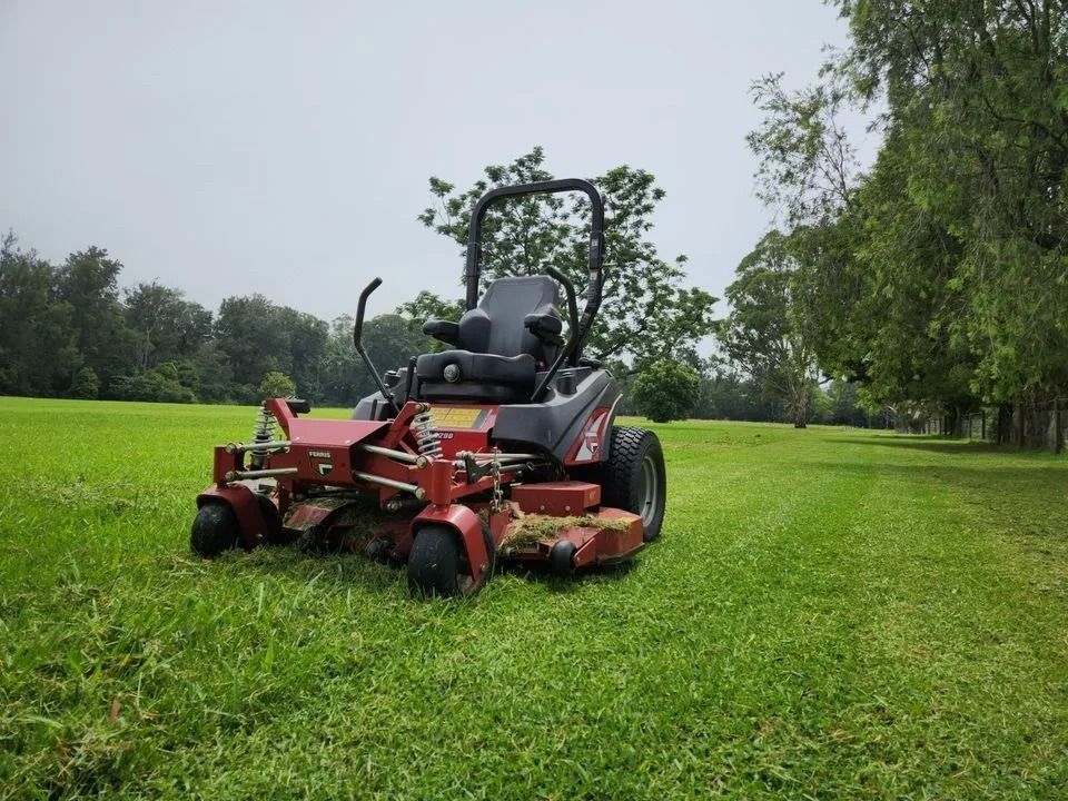 Red zero-turn mower cutting grass in a green field under a cloudy sky — Stockers & Partridge In Raymond Terrace, NSW