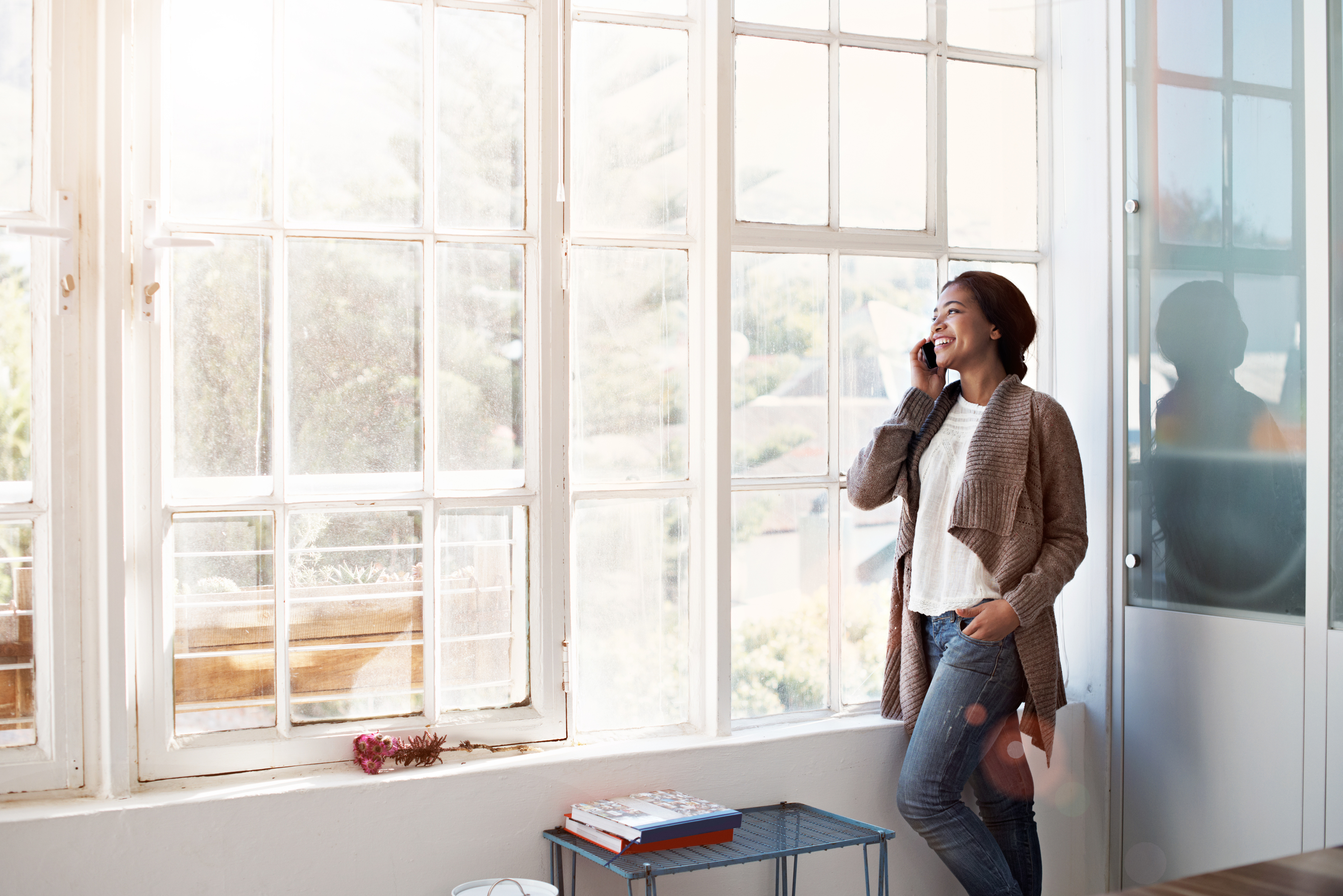 A woman is standing in front of a window talking on a cell phone.