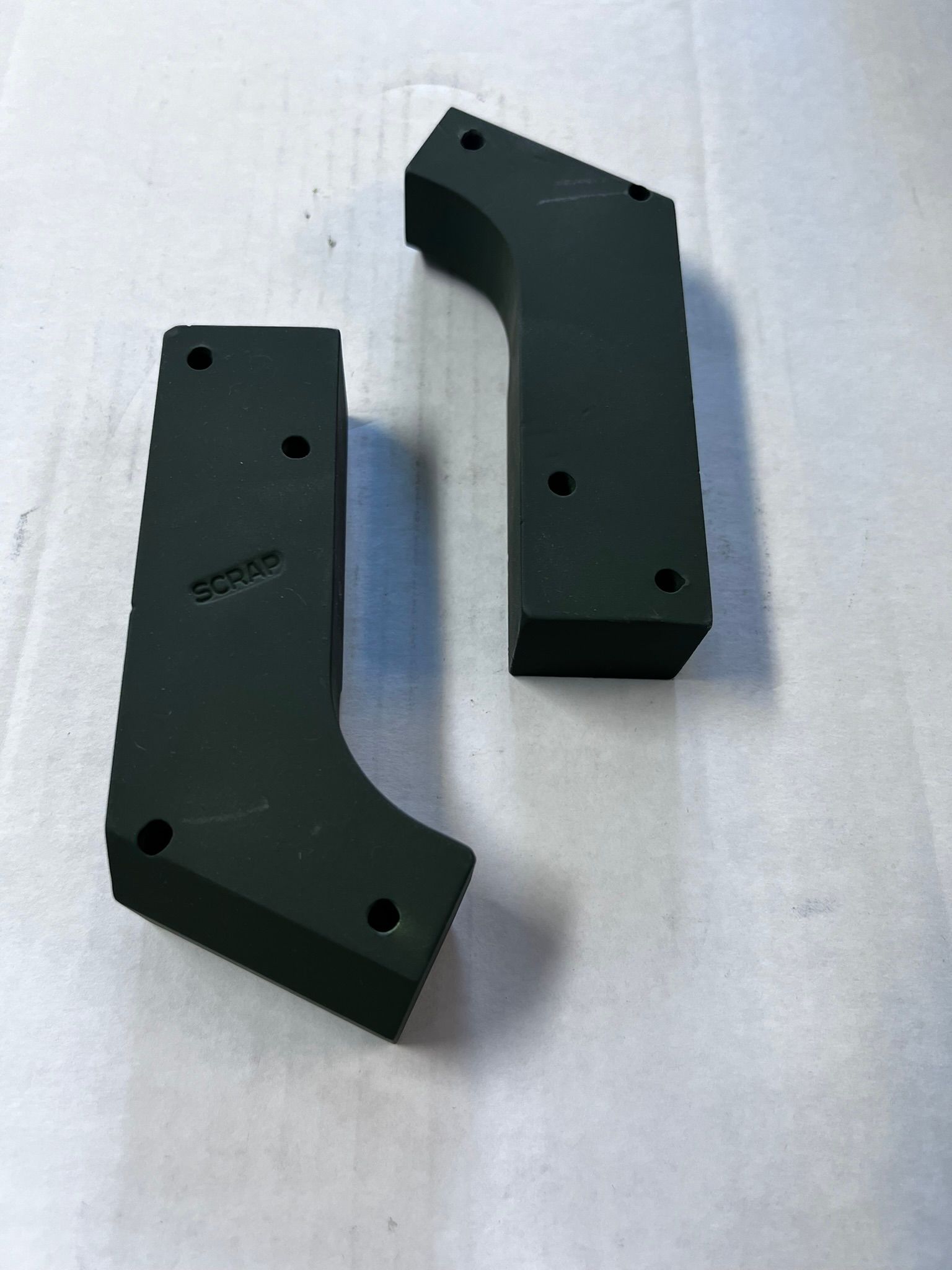 A pair of black plastic pieces with holes in them on a white surface