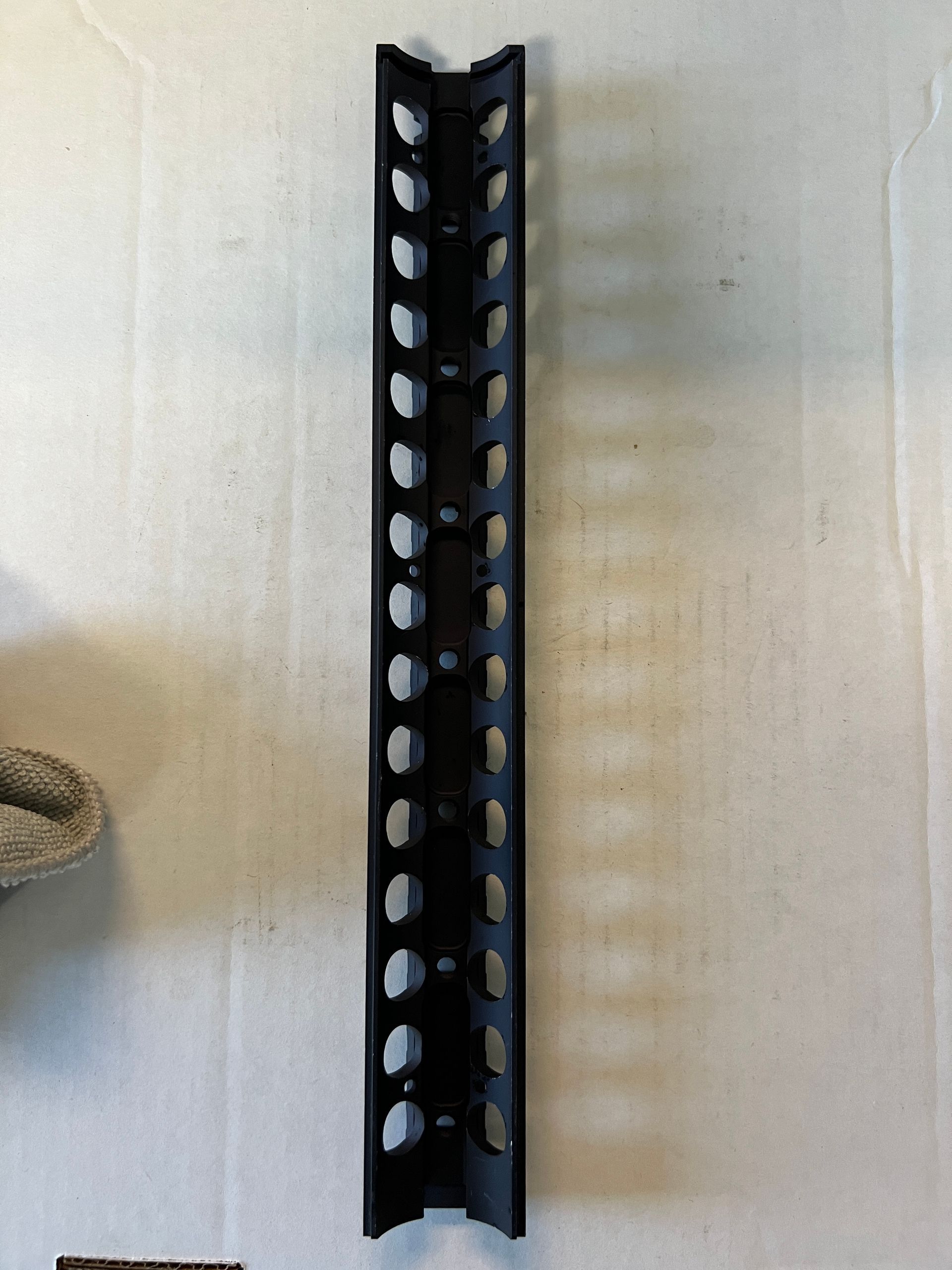 A black metal bar with holes in it is sitting on a white surface.