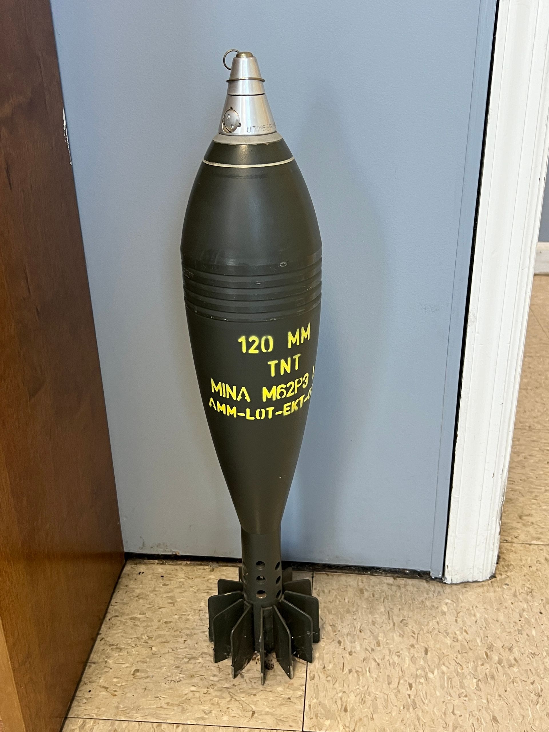 A 120 mm tnt mine is sitting on the floor next to a door.
