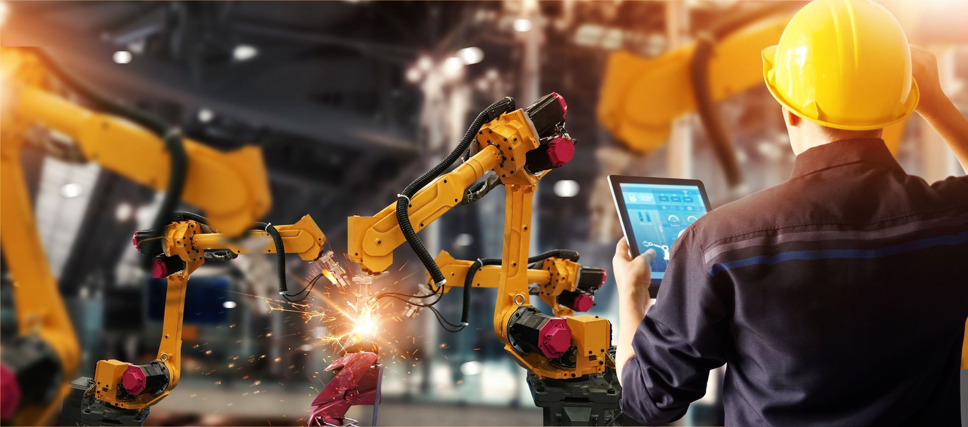 A man in a hard hat is using a tablet in a factory.