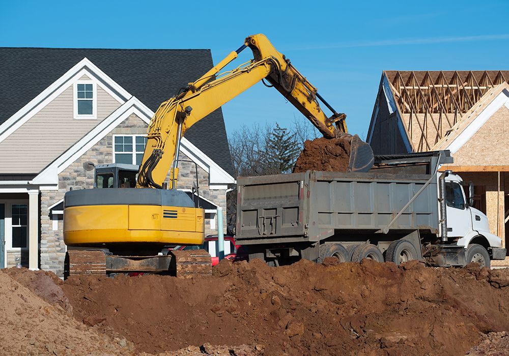 Excavator loading broken concrete into dump trailer during demolition