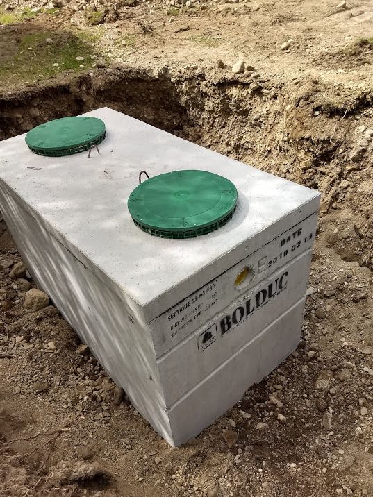 Septic Tank box with two green covers, set in a dirt trench outdoors.