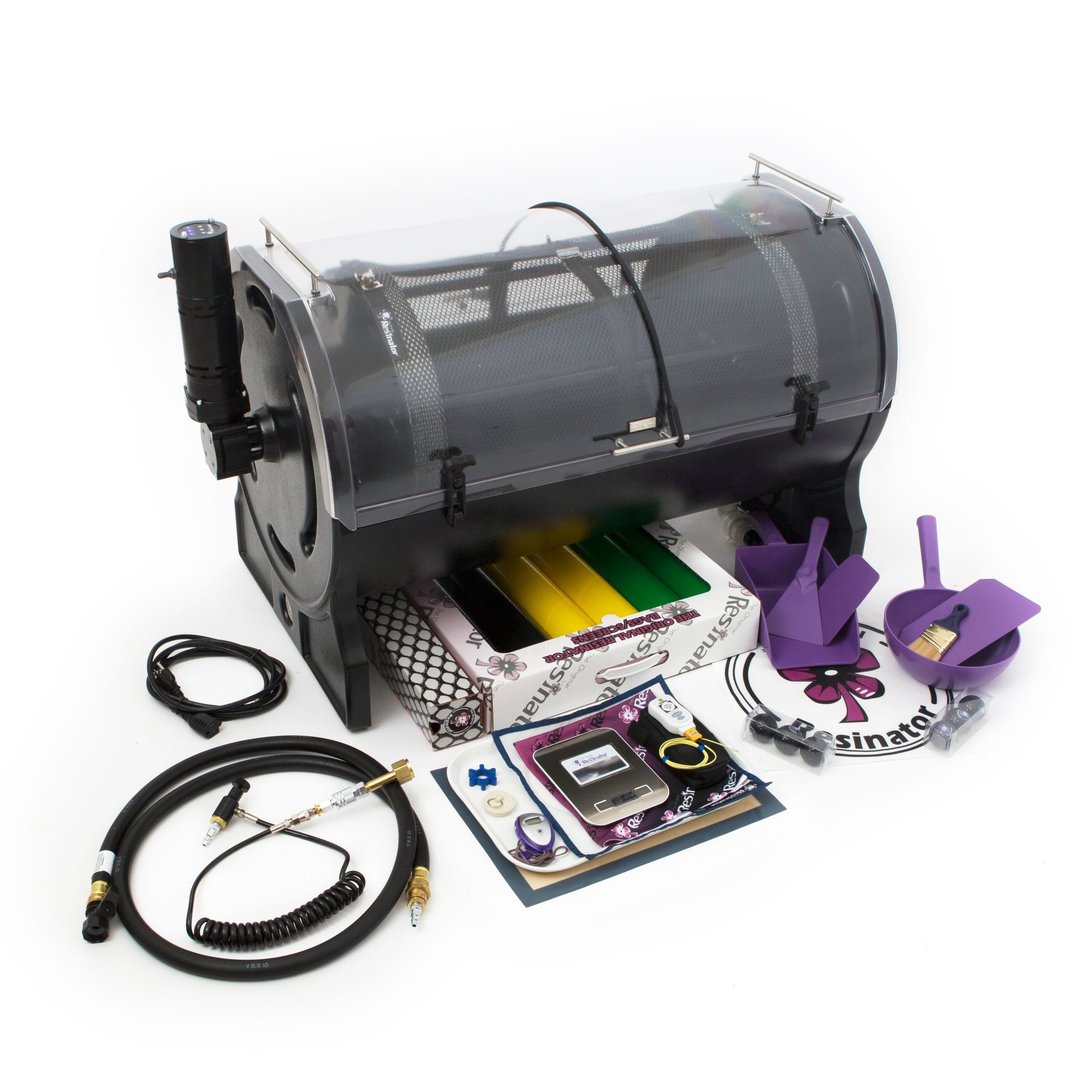 A black motorized tumbler machine with a clear cover, accompanied by cables, small scoops, and accessories on a white floor.
