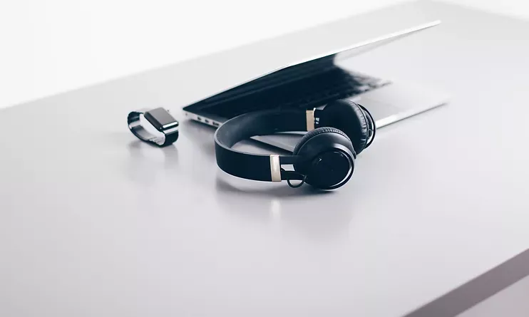 Black over-ear headphones beside a USB flash drive on a white desk with a laptop corner above