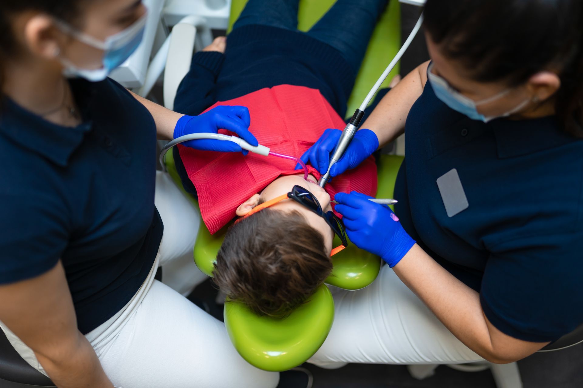 A young boy is laying in a dental chair getting his teeth examined by two dentists.
