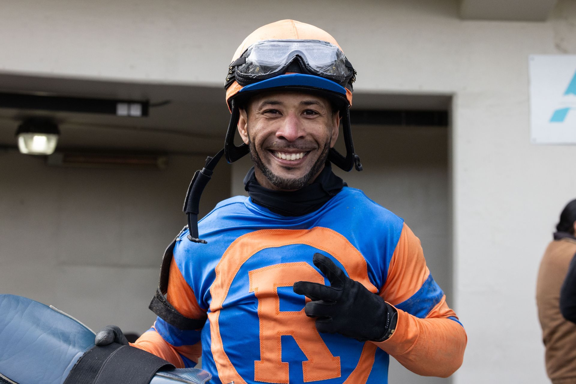 jockey in blue and orange silk smiling and giving a peace sign gesture with hand