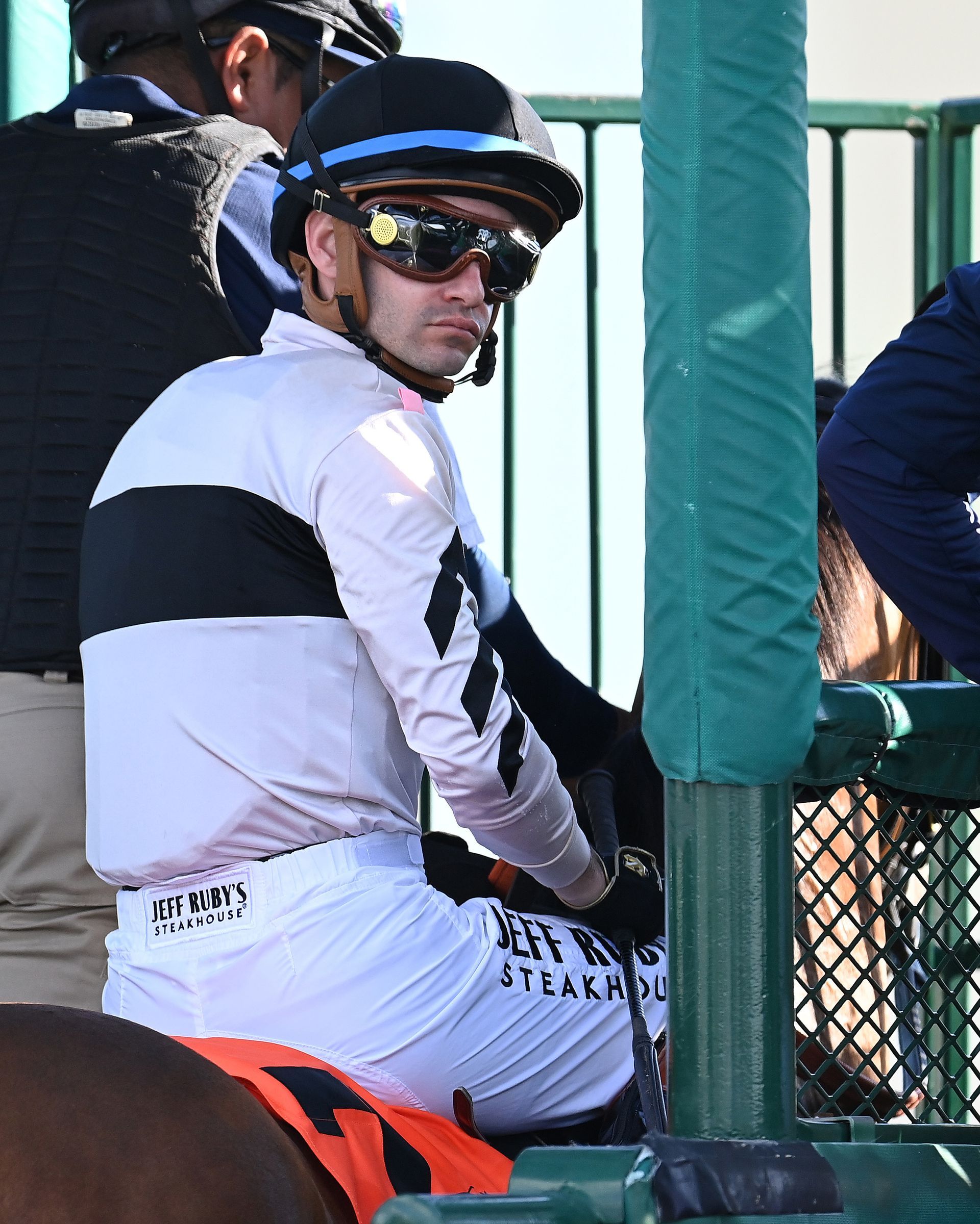 jockey in the starting gate wearing black and white silk looks at camera