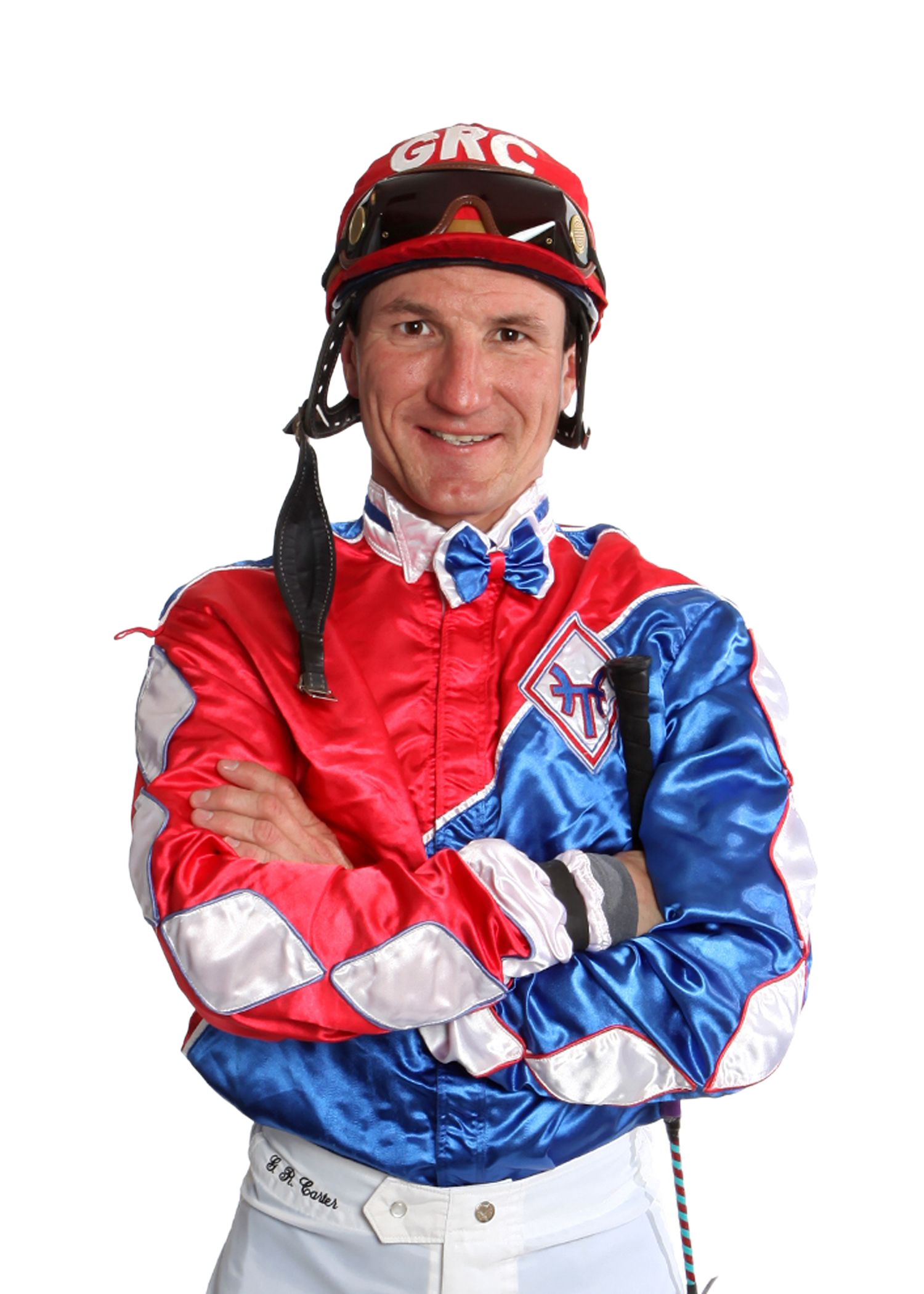 Jockey in red and blue racing silks, wearing a helmet, standing with arms crossed and smiling.