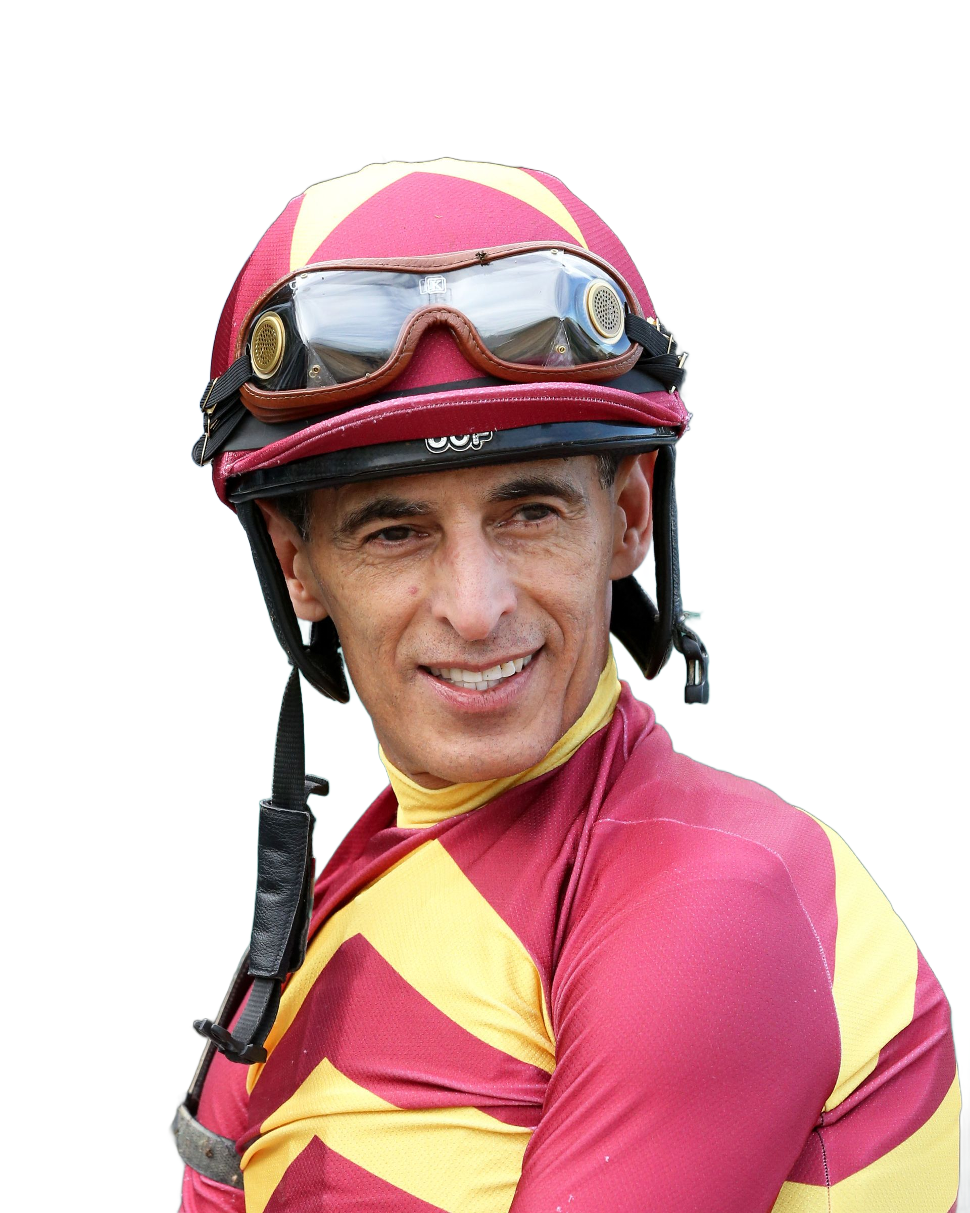 A jockey in a white racing outfit and helmet with goggles, looking toward the camera at a racetrack.