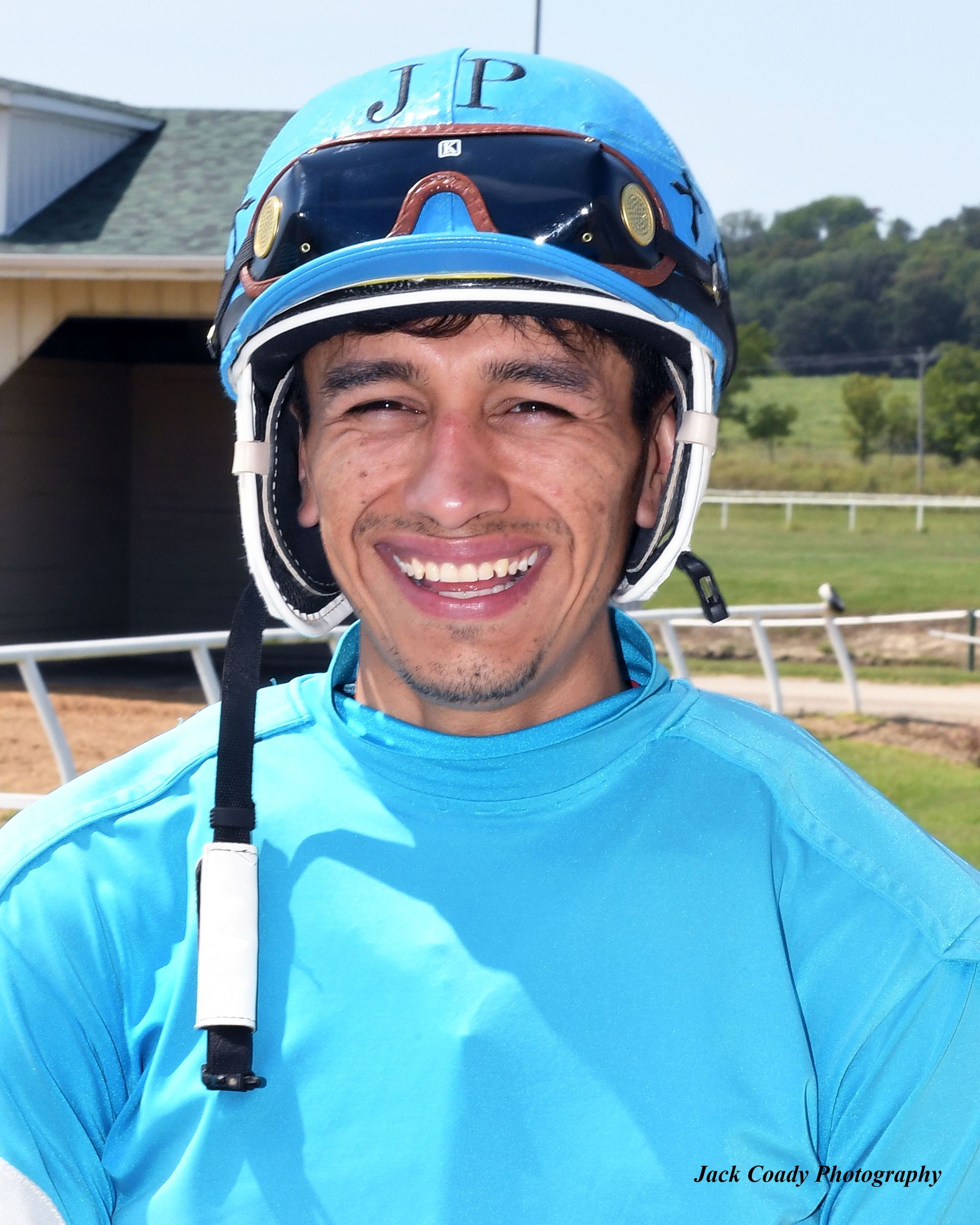 Smiling jockey in blue helmet and silks standing outdoors on a racetrack