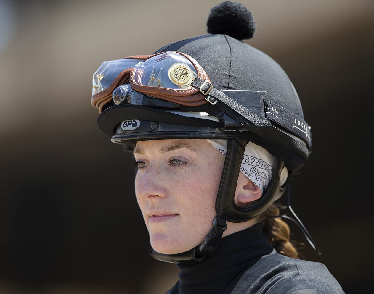 Jockey Jessica Pyfer wearing a black helmet , protective goggles, and a dark 
turtleneck, looking off to the side.