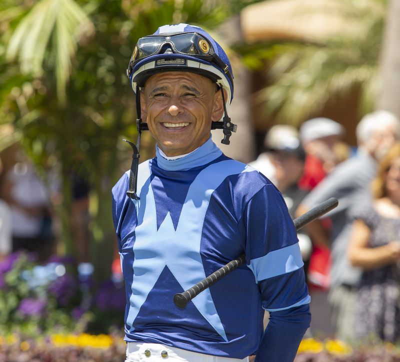 Jockey Mike Smith in a blue and light blue racing uniform and helmet, outdoors at a track.
