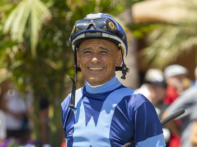Smiling jockey in blue racing silks and helmet at an outdoor racetrack