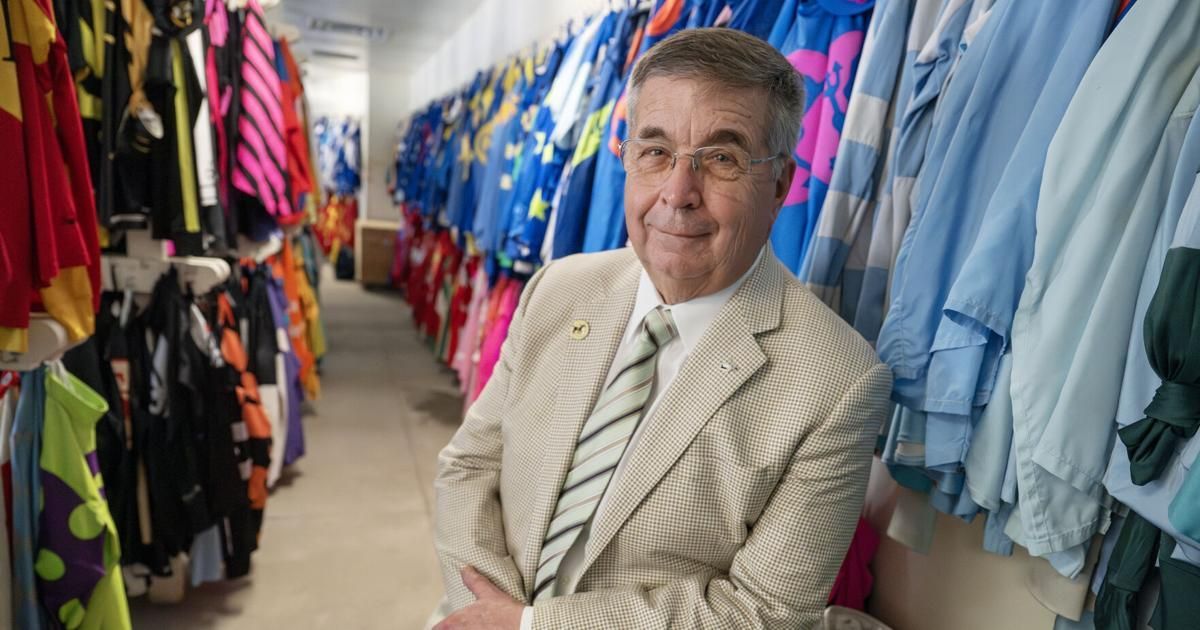 Man standing in a clothing store aisle, surrounded by colorful shirts and light blue garments.