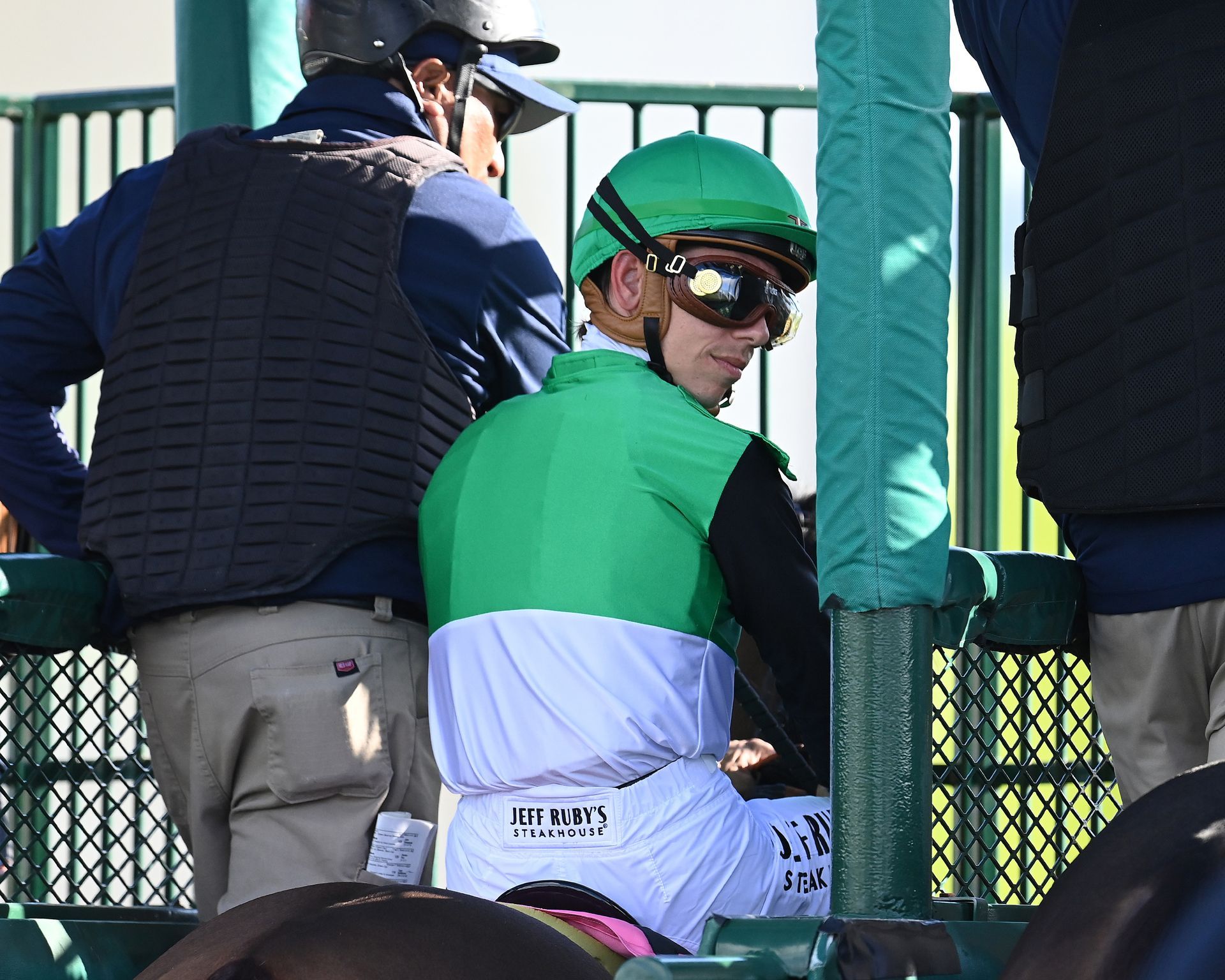 jockey in starting gate wearing green silk looking back toward the camera