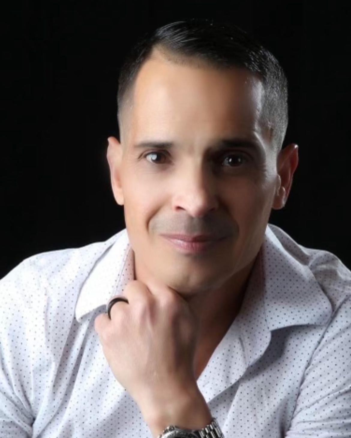 Portrait of a person in a white shirt, resting chin on hand against a black background