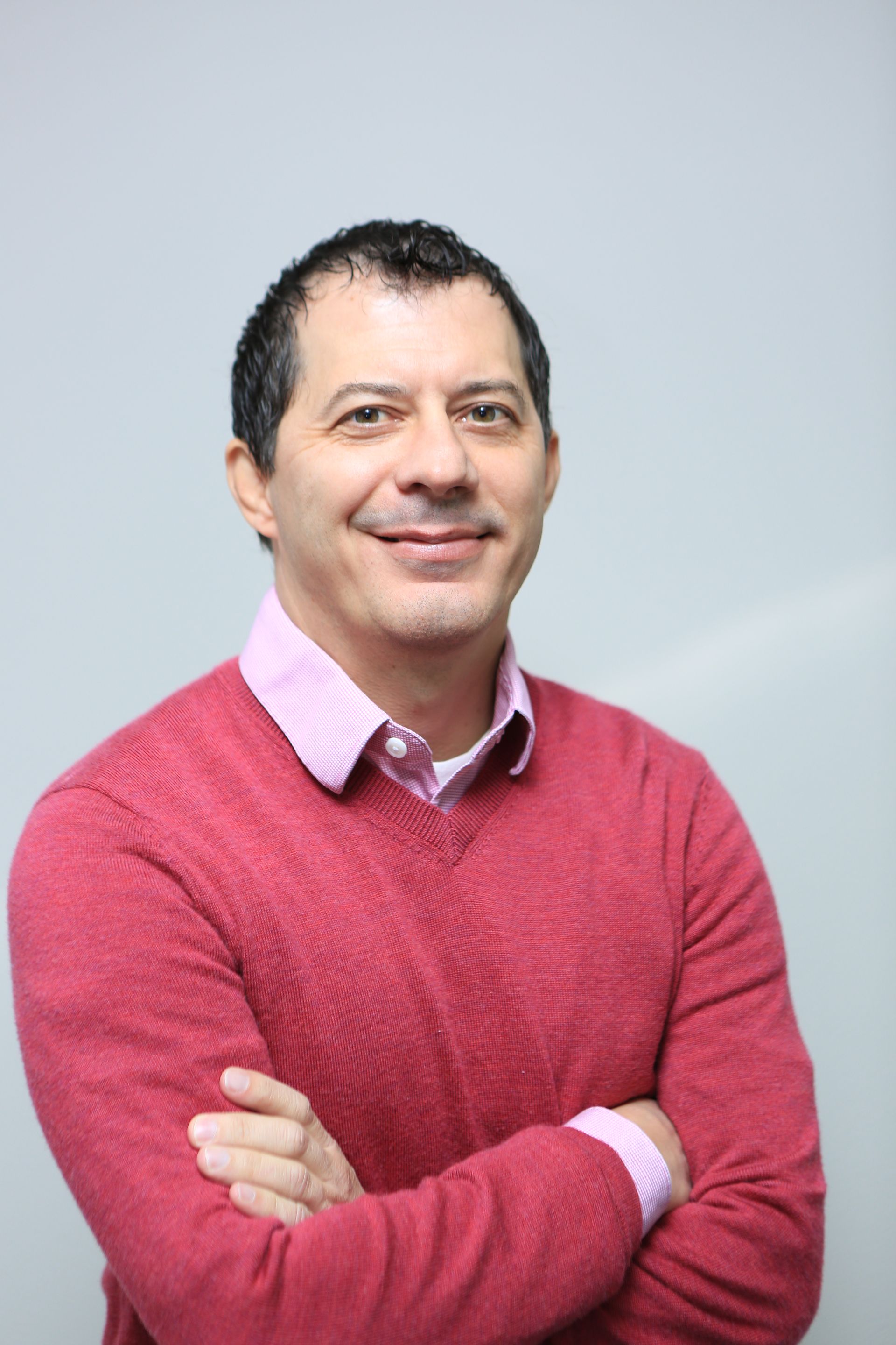 Man in a pink sweater standing with arms crossed against a light gray background
