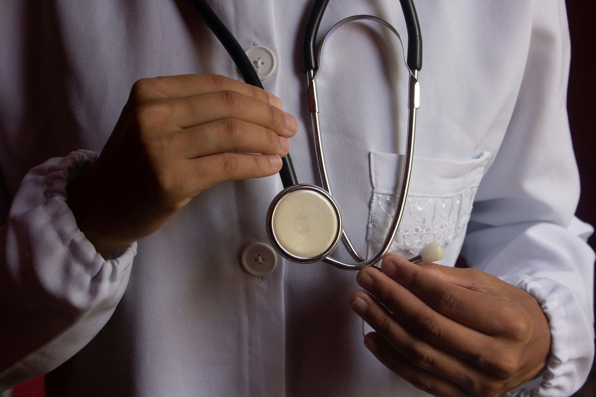 A healthcare professional wearing a white coat holds a stethoscope in their hands.