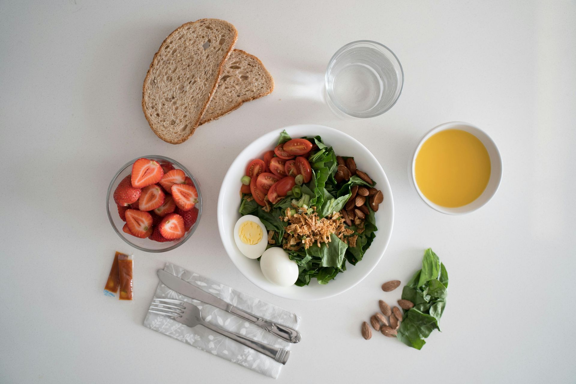 Breakfast spread with salad, strawberries, bread, orange juice, and a glass of water on a white table