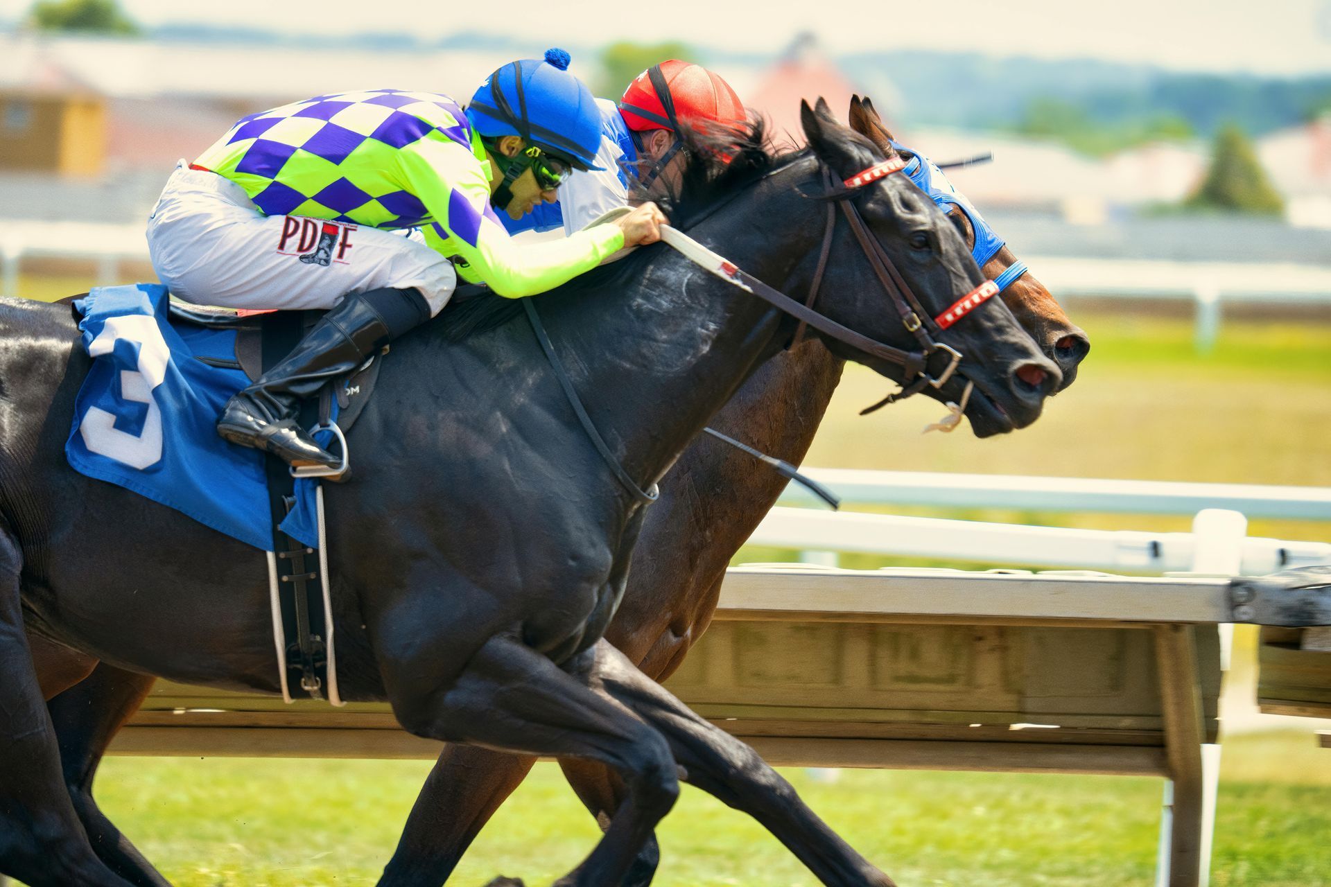Two jockeys in colorful silks ride black horses side-by-side during a horse race on an outdoor track.