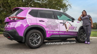 Woman in scrubs leans on a purple car.
