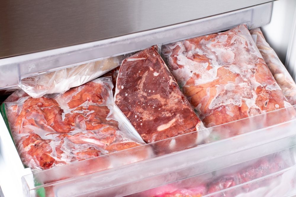 Frozen raw meat packages in a freezer drawer under a frosted lid