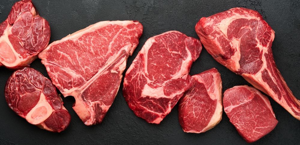 Assorted raw beef cuts on a dark surface, marbled red meat arranged in a row