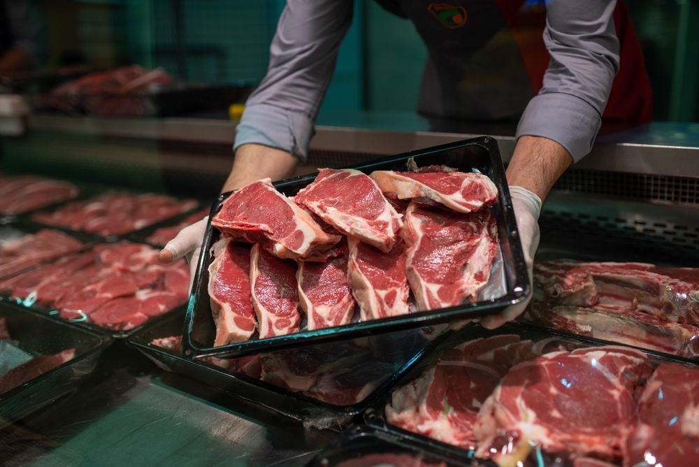 Butcher holding tray of raw steaks in a meat market counter