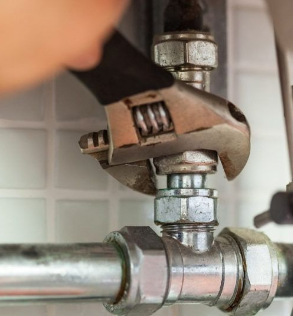 Hand with wrench tightening a fitting on plumbing pipes.