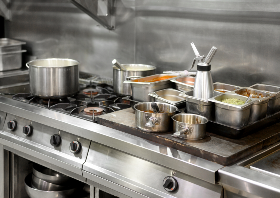 Stainless steel commercial kitchen with pots, pans, and containers on a stovetop.