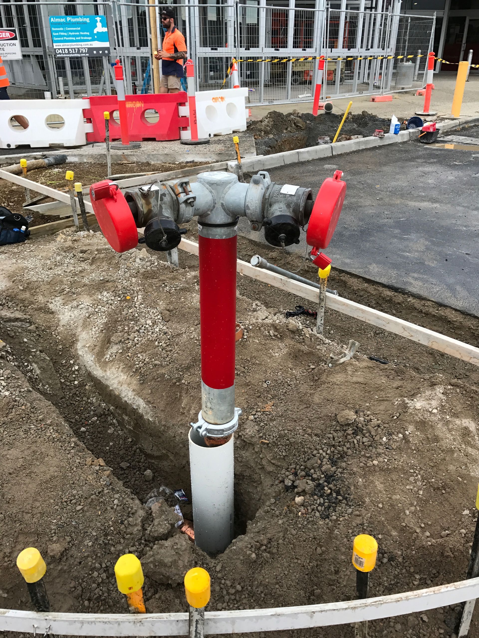 A red and silver fire hydrant in a dirt excavation with construction markers nearby.