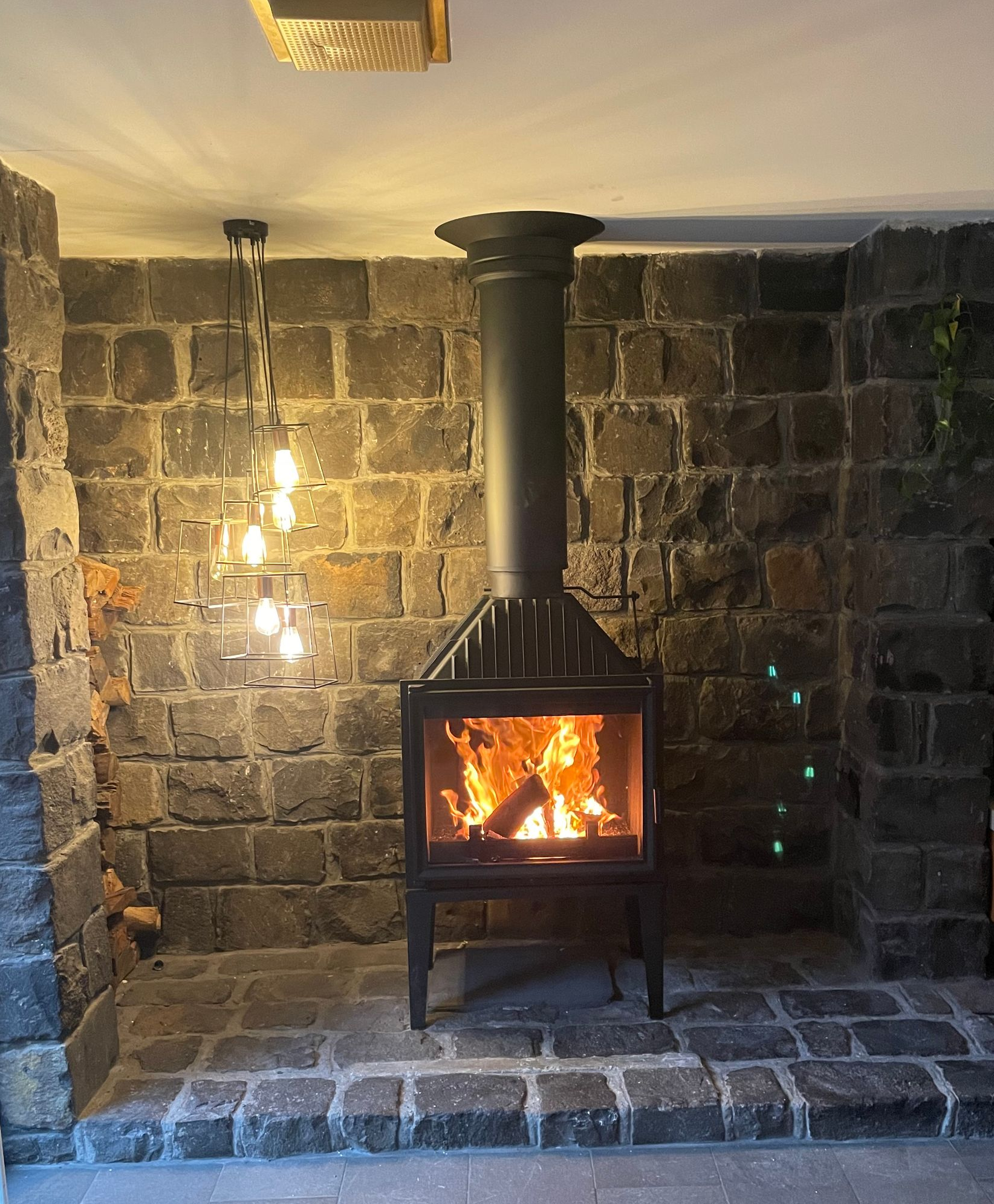 Fireplace with flames in a stone-walled room, with a decorative light fixture and chimney.