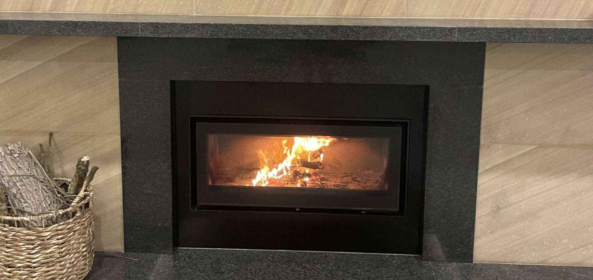 A fireplace with a burning fire, surrounded by black stone and light wood paneling.